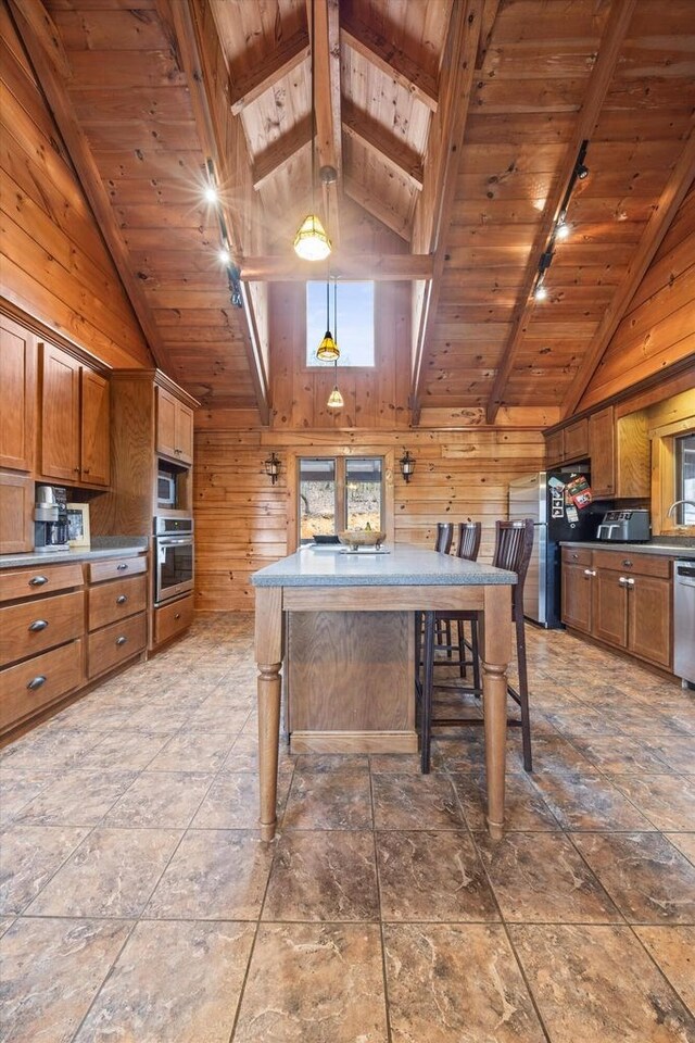 kitchen with appliances with stainless steel finishes, wooden walls, beamed ceiling, a center island, and wooden ceiling