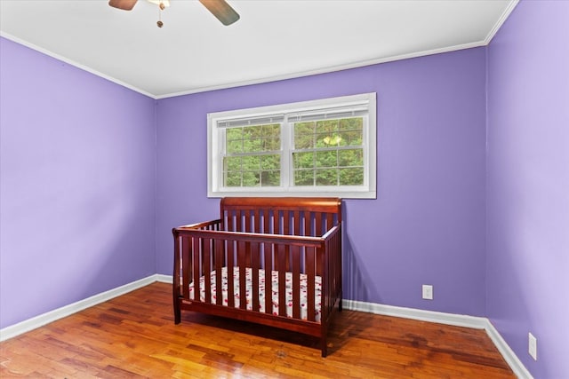 bedroom featuring ornamental molding, a nursery area, hardwood / wood-style floors, and ceiling fan