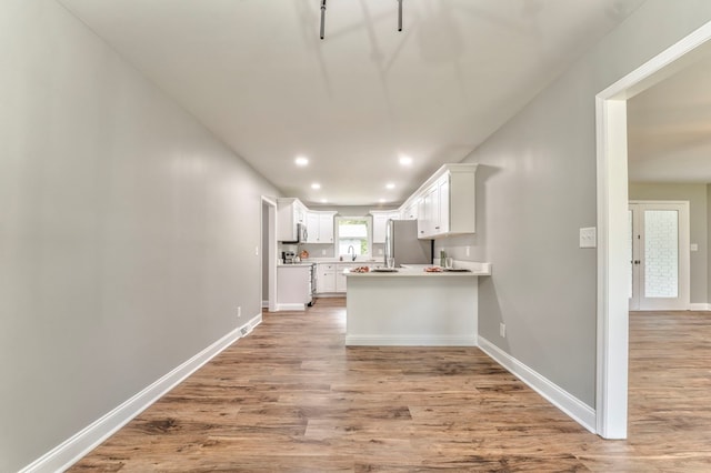 kitchen with range, stainless steel refrigerator, kitchen peninsula, hardwood / wood-style flooring, and white cabinets