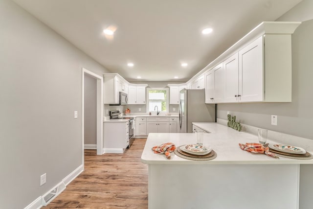 kitchen with stainless steel appliances, kitchen peninsula, white cabinets, and light wood-type flooring