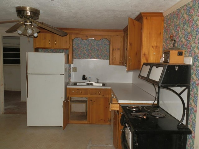 kitchen with brown cabinets, freestanding refrigerator, a textured ceiling, a ceiling fan, and a sink