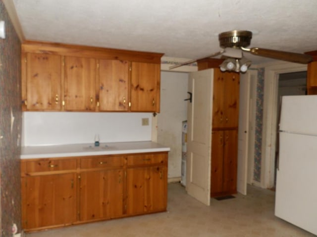 kitchen with brown cabinetry, light countertops, freestanding refrigerator, and a ceiling fan