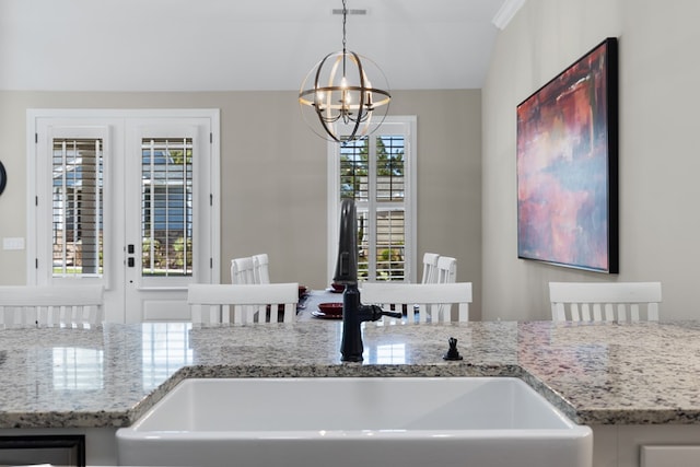 kitchen with light stone counters, sink, hanging light fixtures, and a notable chandelier