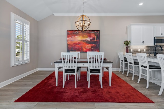 dining area featuring lofted ceiling, sink, light hardwood / wood-style flooring, and a chandelier