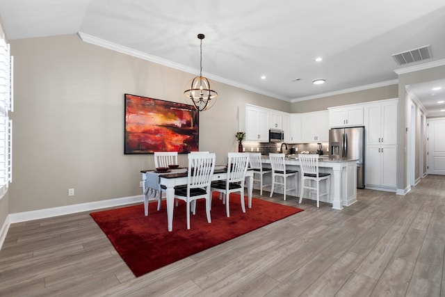 dining area with crown molding, a chandelier, vaulted ceiling, and light wood-type flooring