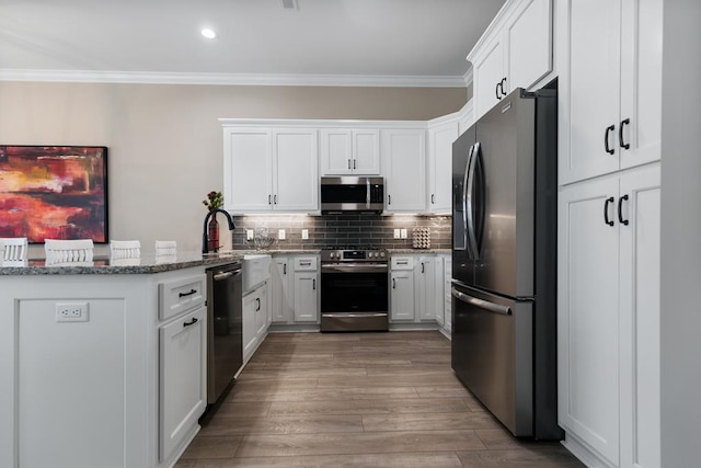 kitchen with white cabinetry, ornamental molding, appliances with stainless steel finishes, light stone countertops, and decorative backsplash