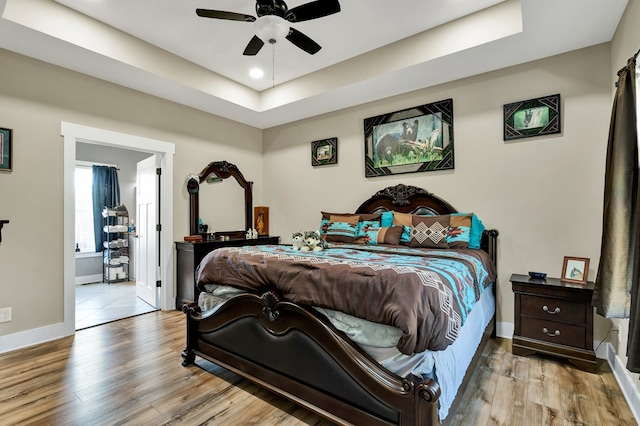 bedroom featuring ceiling fan, light wood-type flooring, and a tray ceiling