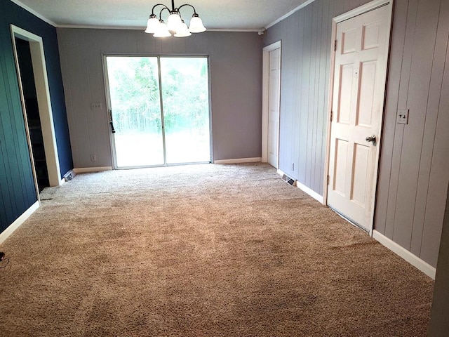 empty room with crown molding, an inviting chandelier, wooden walls, and carpet floors