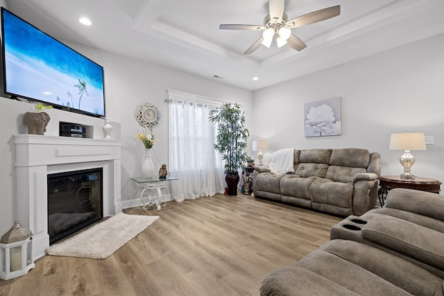 living room featuring a tray ceiling, ceiling fan, and light hardwood / wood-style floors