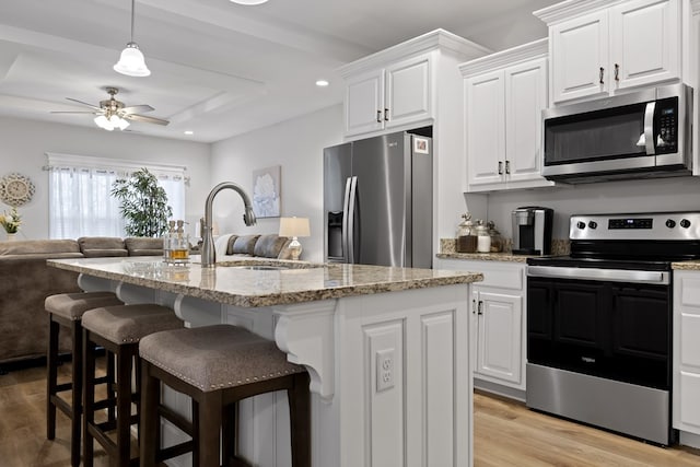 kitchen featuring appliances with stainless steel finishes, a kitchen island with sink, white cabinets, and light stone counters