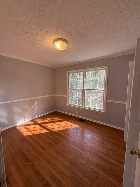 empty room with ornamental molding, hardwood / wood-style floors, and a textured ceiling