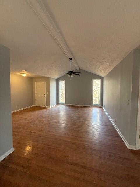 unfurnished living room with vaulted ceiling with beams, a wealth of natural light, dark hardwood / wood-style floors, and ceiling fan