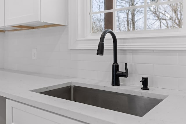 room details featuring light stone counters, white cabinetry, sink, and tasteful backsplash