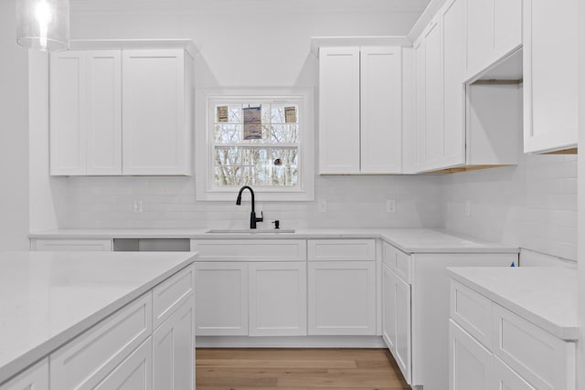 kitchen featuring white cabinetry, sink, light wood-type flooring, and decorative light fixtures