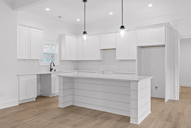 kitchen featuring a center island, ornamental molding, pendant lighting, light hardwood / wood-style floors, and white cabinets