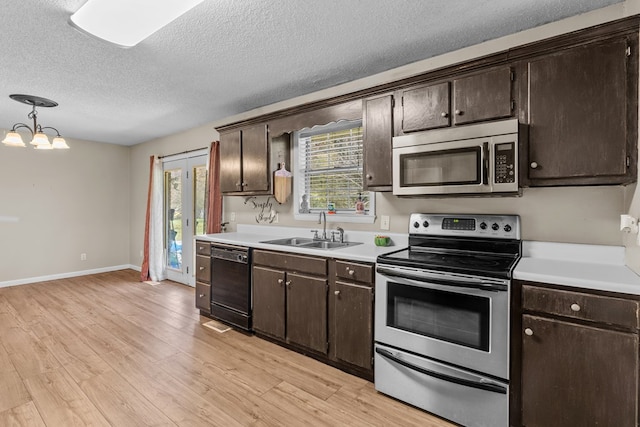 kitchen with pendant lighting, sink, stainless steel appliances, dark brown cabinetry, and light hardwood / wood-style floors