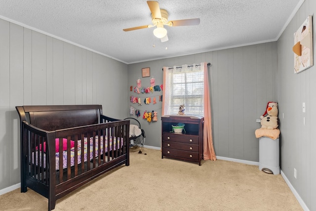 bedroom with a nursery area, ornamental molding, ceiling fan, light carpet, and a textured ceiling