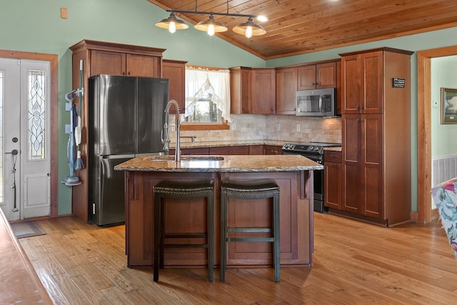 kitchen featuring an island with sink, light stone counters, appliances with stainless steel finishes, a breakfast bar, and a sink