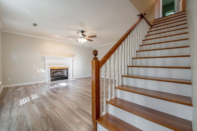 stairway with crown molding, ceiling fan, hardwood / wood-style flooring, and a textured ceiling