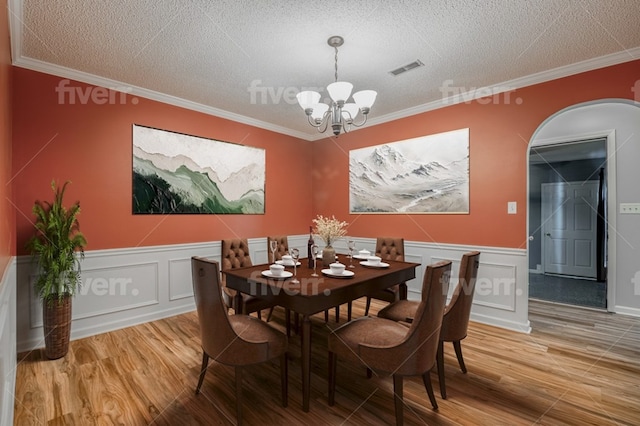 dining space featuring ornamental molding, hardwood / wood-style floors, a notable chandelier, and a textured ceiling