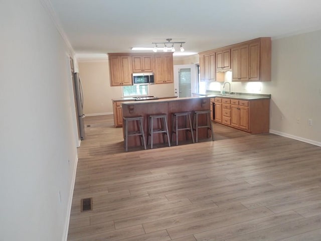 kitchen with crown molding, light hardwood / wood-style flooring, a kitchen breakfast bar, stainless steel appliances, and a center island