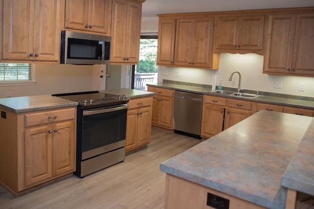 kitchen featuring appliances with stainless steel finishes, sink, ornamental molding, a center island, and light wood-type flooring