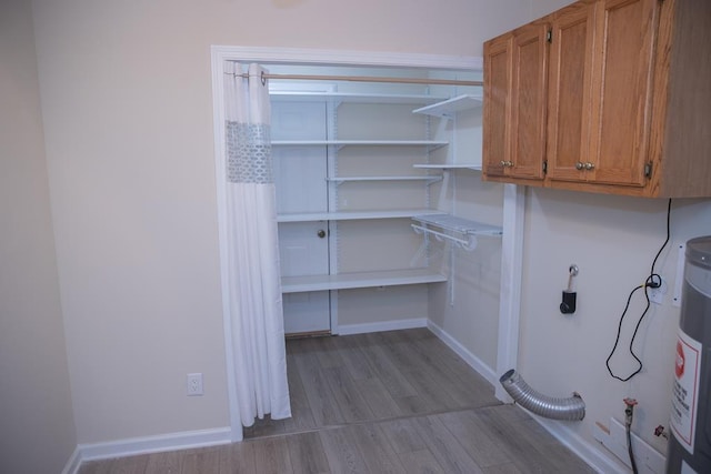 clothes washing area featuring cabinets, hookup for an electric dryer, water heater, and light hardwood / wood-style flooring