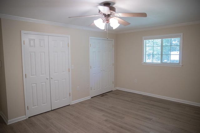 unfurnished bedroom featuring ceiling fan, light hardwood / wood-style flooring, ornamental molding, and multiple closets