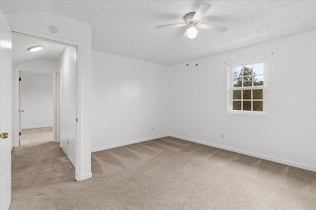 unfurnished room with a ceiling fan, baseboards, vaulted ceiling, a textured ceiling, and light carpet