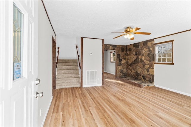 unfurnished living room with visible vents, ceiling fan, stairway, light wood-style floors, and a textured ceiling