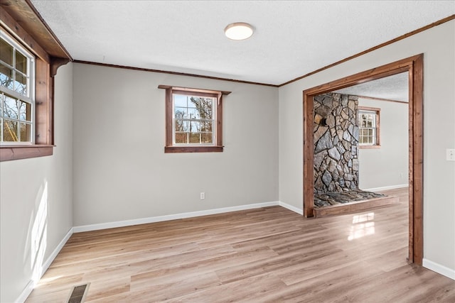 spare room featuring baseboards, visible vents, light wood finished floors, ornamental molding, and a textured ceiling