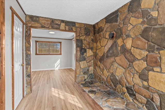 hall featuring light wood-style flooring, a textured ceiling, and baseboards