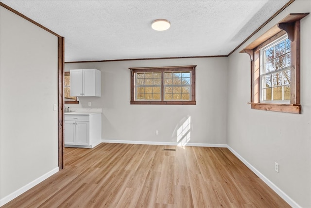 unfurnished room featuring baseboards, a textured ceiling, crown molding, and light wood finished floors