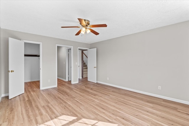 unfurnished bedroom with a walk in closet, baseboards, light wood-type flooring, a textured ceiling, and a ceiling fan