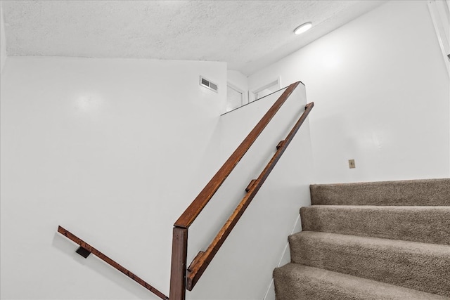 staircase featuring visible vents, lofted ceiling, and a textured ceiling