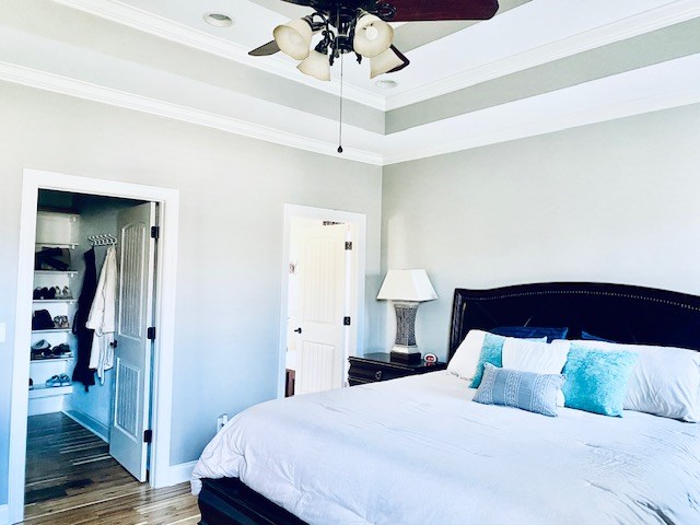 bedroom featuring ornamental molding, a tray ceiling, a ceiling fan, and wood finished floors