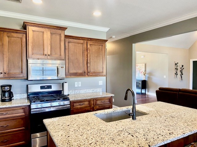 kitchen with light stone counters, a kitchen island with sink, a sink, appliances with stainless steel finishes, and crown molding