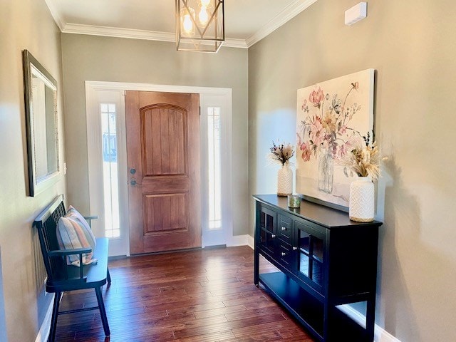 foyer entrance featuring a notable chandelier, ornamental molding, dark wood finished floors, and baseboards