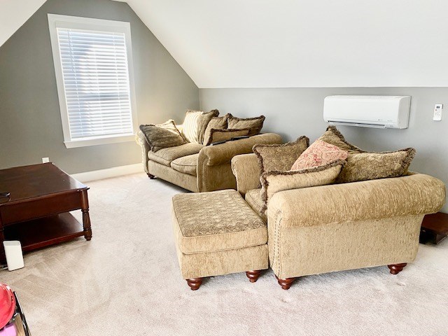 carpeted living area featuring vaulted ceiling, a wall mounted air conditioner, and baseboards