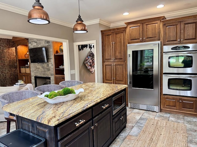 kitchen featuring crown molding, stainless steel appliances, a center island, light stone countertops, and a stone fireplace