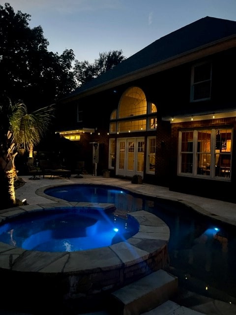 pool at dusk with an in ground hot tub, a patio area, and french doors