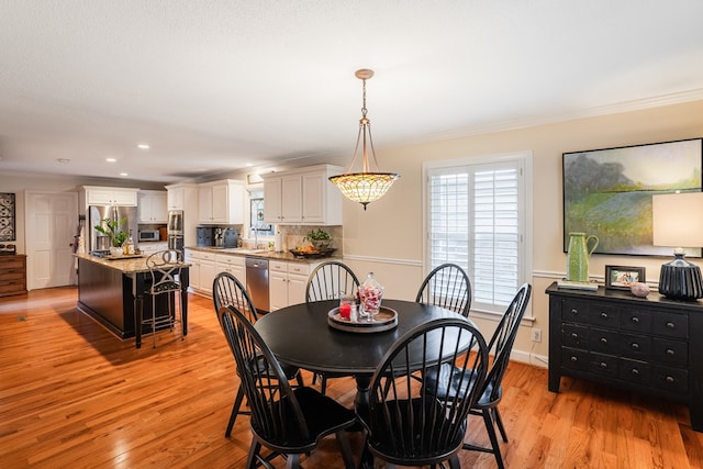 dining area with crown molding, sink, and light wood-type flooring