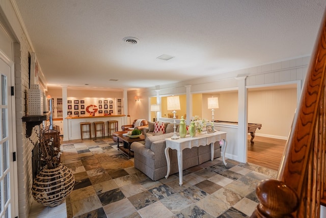 living room with a brick fireplace, decorative columns, and a textured ceiling