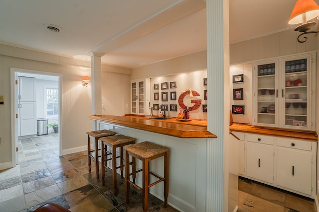 kitchen featuring white cabinetry, ornamental molding, wooden counters, and a kitchen bar