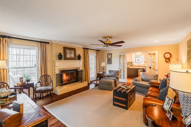 living room with a brick fireplace, wood-type flooring, ornamental molding, and ceiling fan