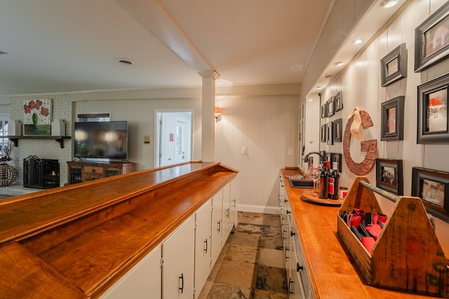 bar with butcher block countertops, sink, white cabinetry, a brick fireplace, and ornate columns