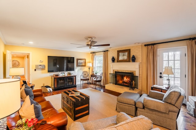 living room with a brick fireplace, crown molding, hardwood / wood-style floors, and ceiling fan