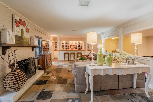 living room with a brick fireplace, crown molding, decorative columns, and brick wall