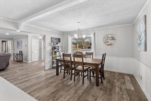 dining area featuring crown molding, wood-type flooring, a chandelier, and a textured ceiling