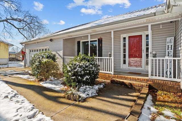 snow covered property entrance with a garage and a porch